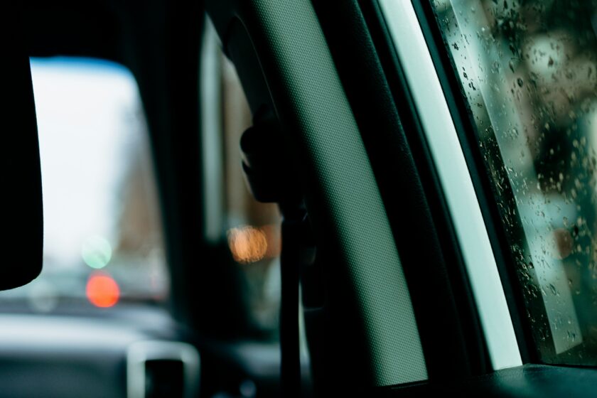 Close-up van de binnenkant van een auto met regendruppels op het raam en een wazig uitzicht naar buiten.